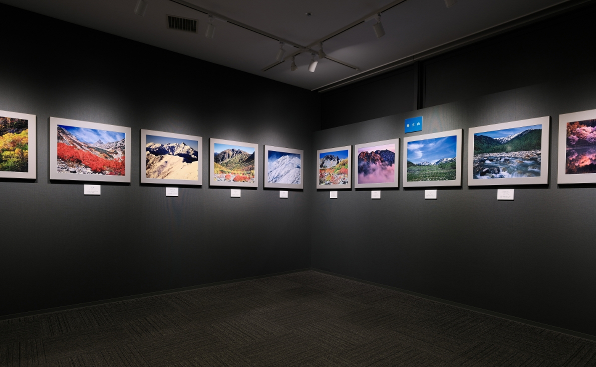 写真展会場で展示作品を指しながら話す石橋修致様と奥様